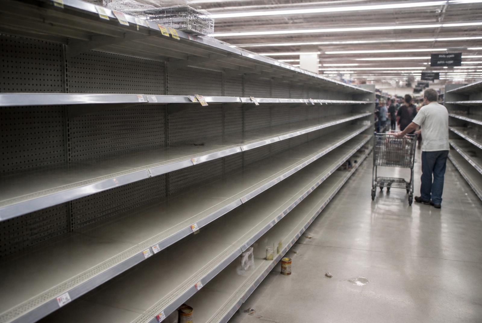 Corsia di supermercato con scaffali completamente vuoti e un cliente con il carrello